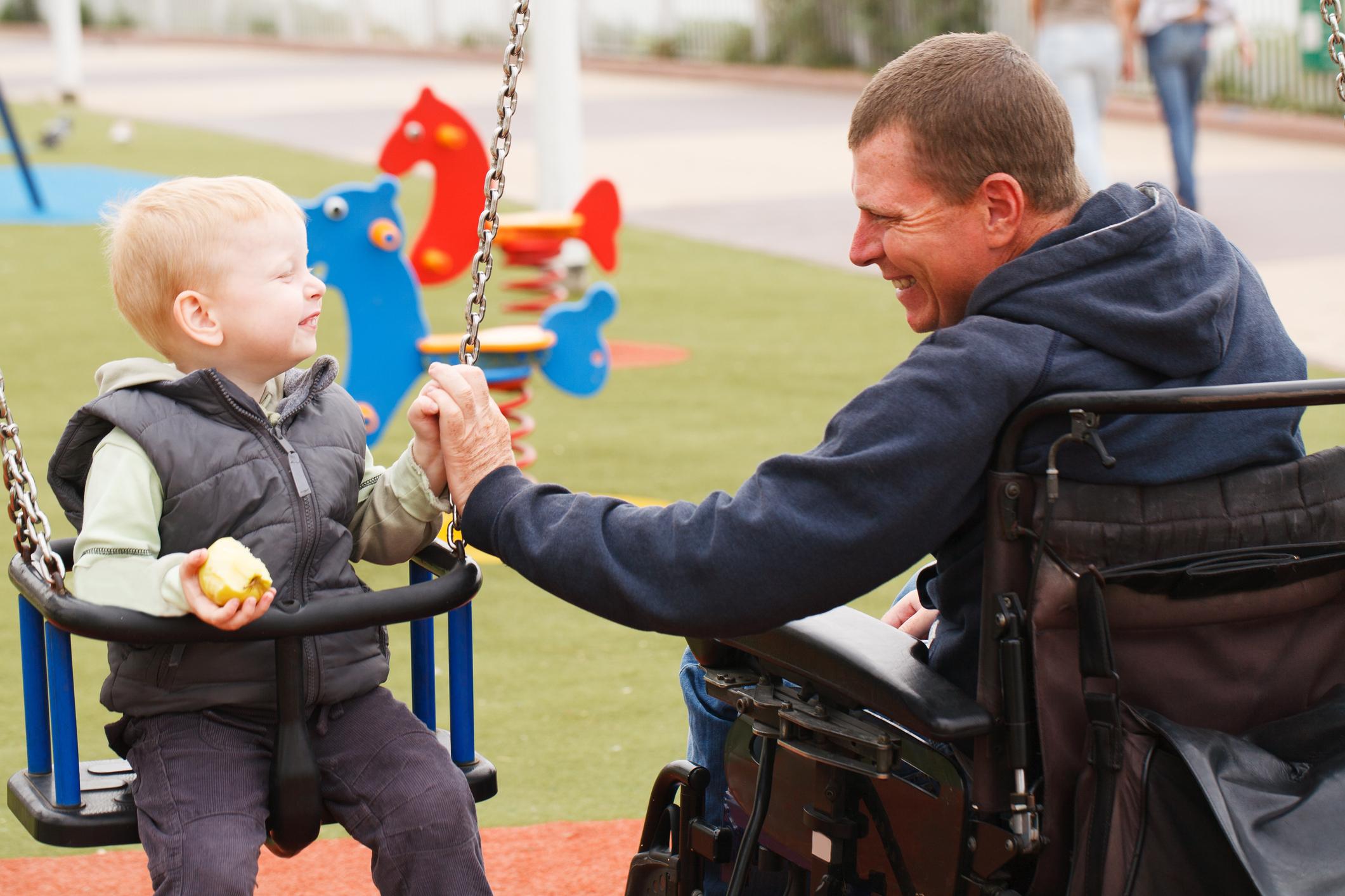 Disabled Father play with his little son on the playground.